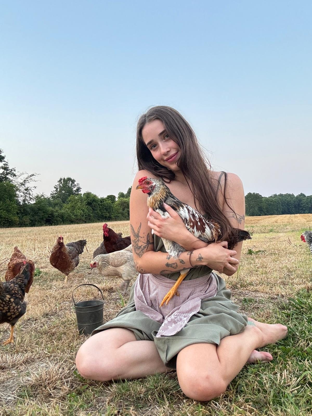 Livinia holding a hen in a field with chickens around her
