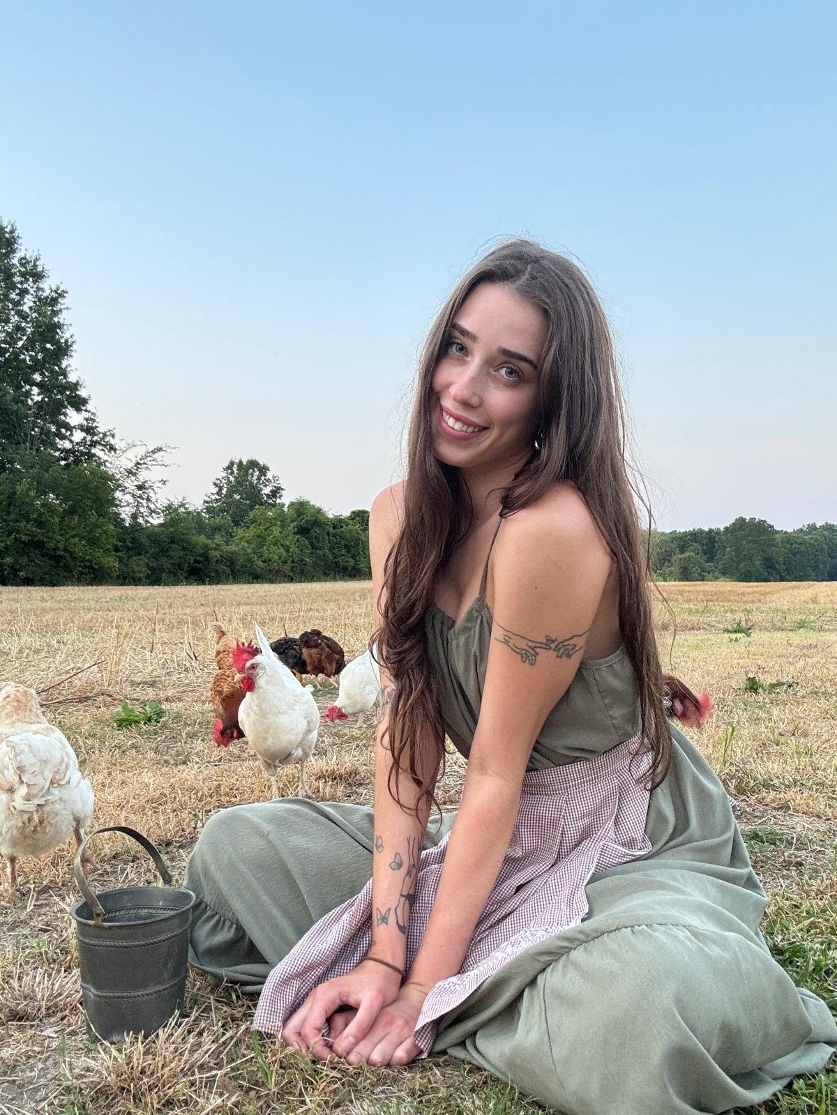 Livinia smiling, sitting in a field with her chickens